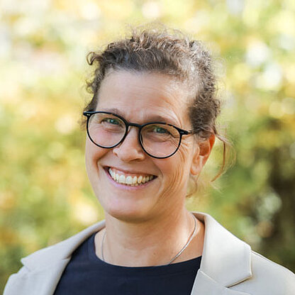 Mitarbeiterfoto vor grünem Hintergrund draußen.