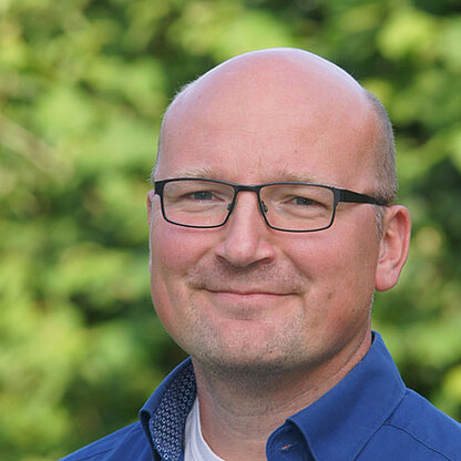 Mitarbeiterfoto vor grünem Hintergrund draußen